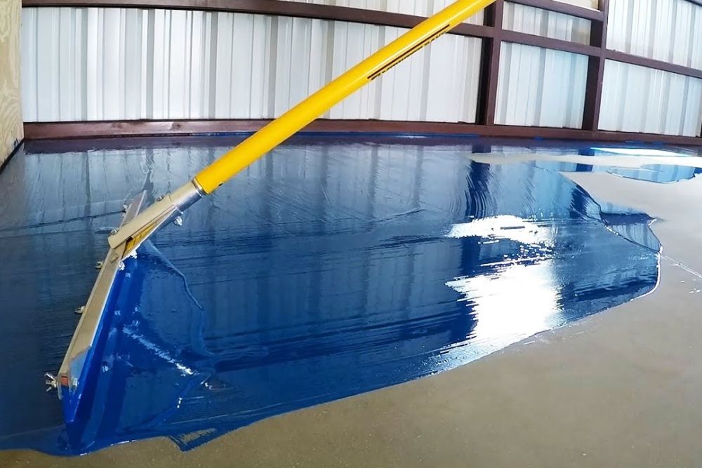 A blue epoxy tile floor with a yellow brush placed on it, highlighting flooring service in Seattle, WA.