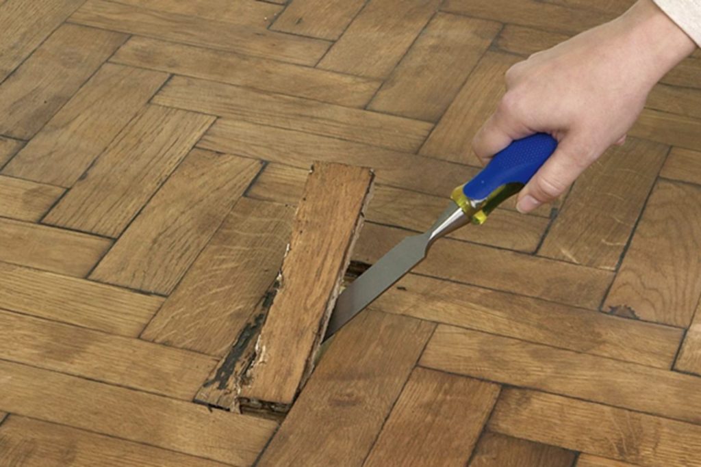Individual using a knife to cut wood on a floor, representing a flooring service based in Seattle, WA.
