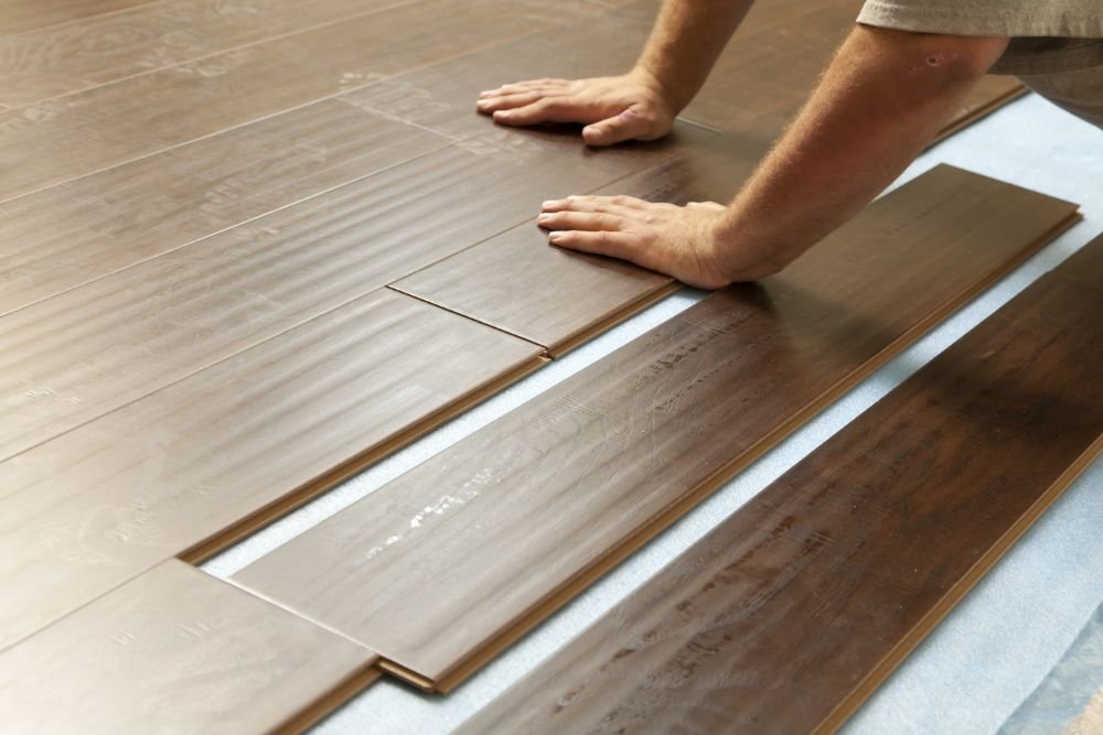 A man carefully laying laminate wood flooring in a Seattle residence, showcasing his craftsmanship and attention to detail.