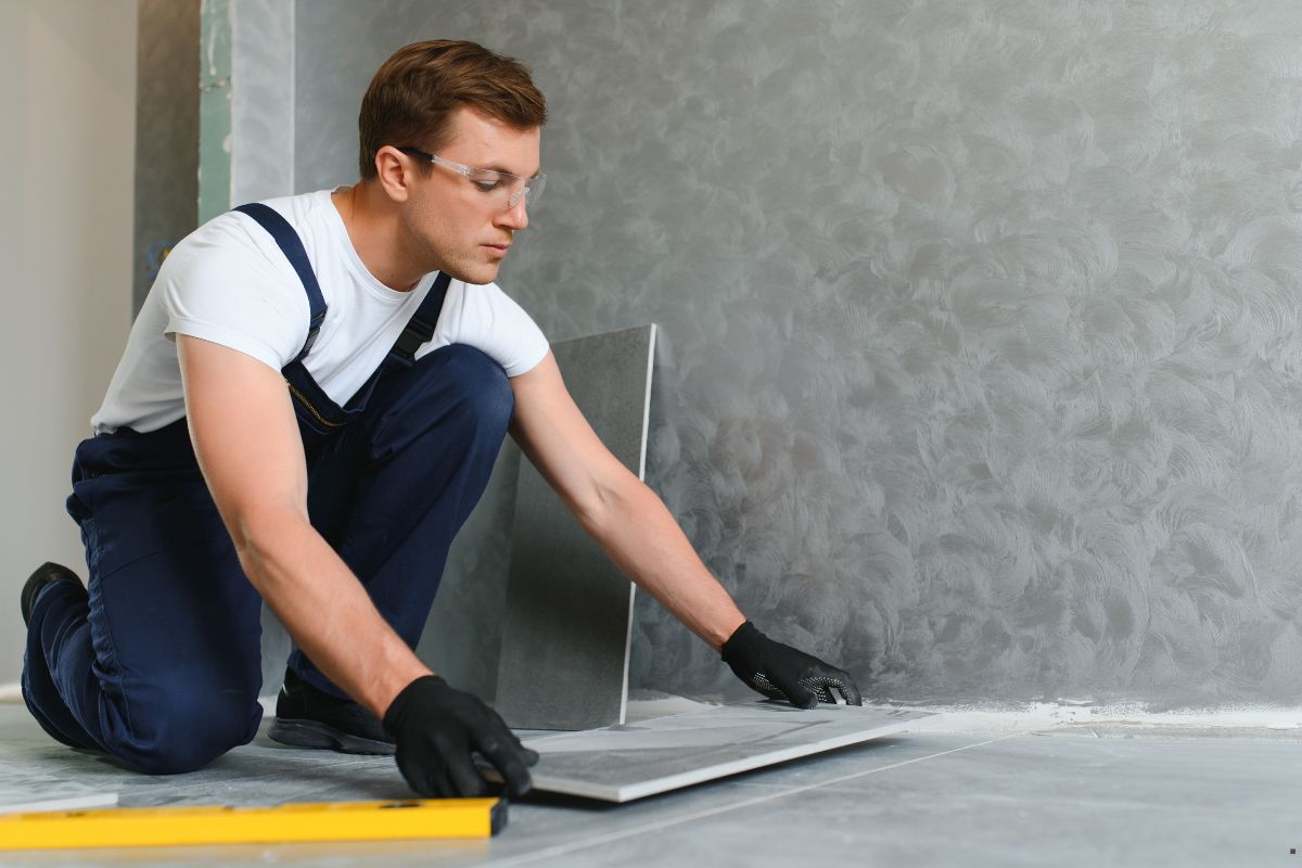A skilled worker in overalls and gloves focuses on installing flooring, highlighting professionalism in flooring services.