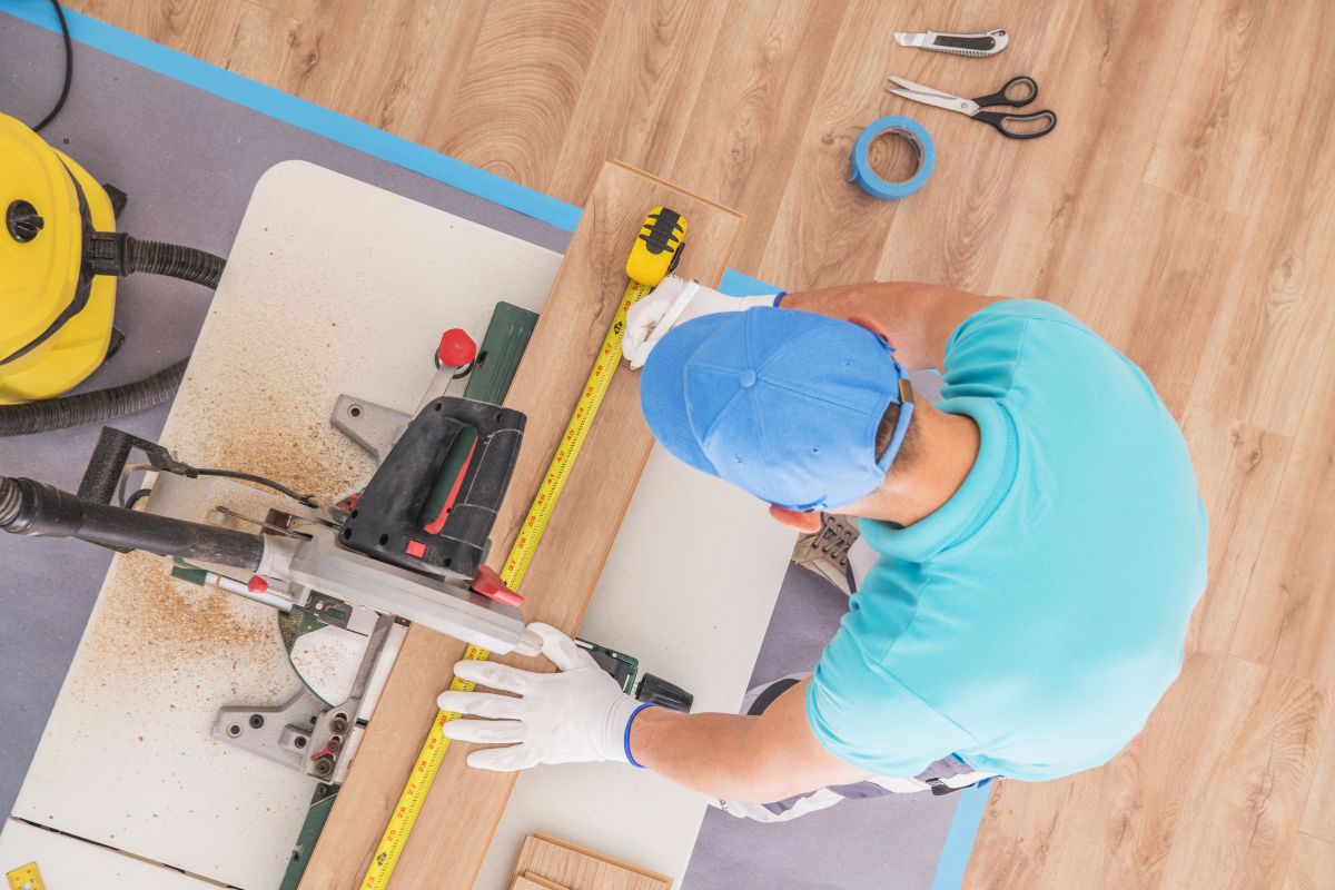 A man using a tool to work on a wooden floor, demonstrating craftsmanship and attention to detail in his task.